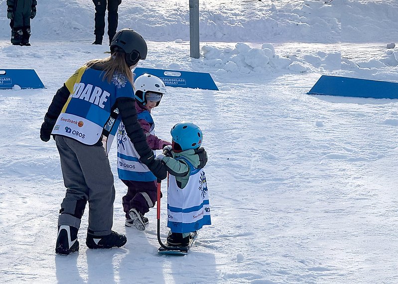 En Alla på snö-ledare hjälper ett litet barn testa snowboard.